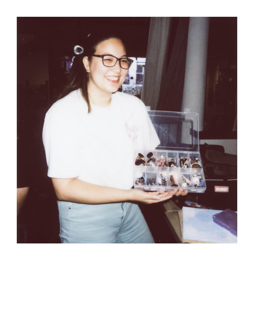 Smiling player holds an organizer filled with painted tabletop RPG miniatures.